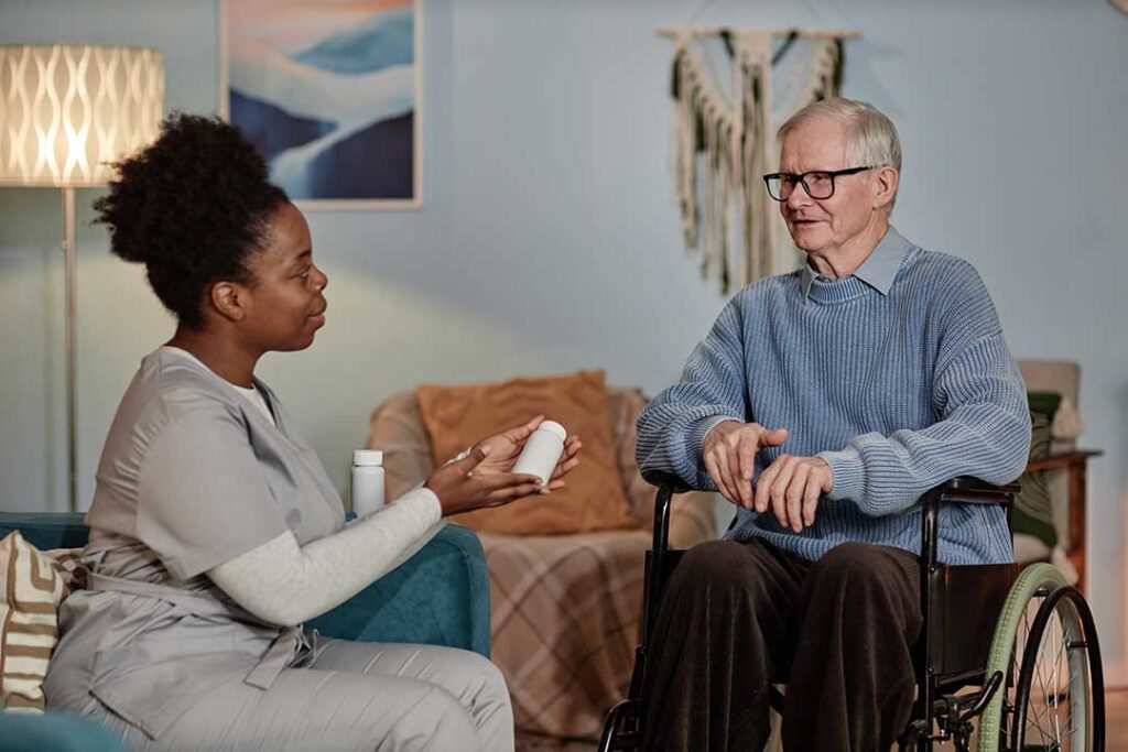 Two older adults sharing tea and conversation at a kitchen table filled with familiar family photos.